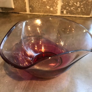 May include: A clear glass bowl with a wavy rim and a deep magenta color.