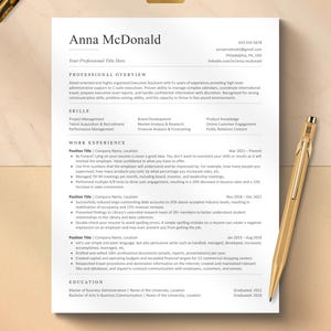 Könnte beinhalten: Eine weiße Lebenslaufvorlage mit dem Namen Anna McDonald in schwarzer Schrift, mit Abschnitten für berufliche Übersicht, Fähigkeiten, Berufserfahrung und Ausbildung. Ein goldener Stift liegt rechts und ein goldenes Etikett zeigt ATS friendly.
