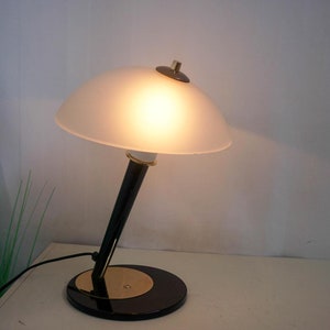 May include: A black and gold desk lamp with a white frosted glass shade. The lamp has a round base and a long, slender stem.