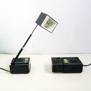 May include: Two black desk lamps with adjustable arms and white lampshades. The lamps have a retro design and are plugged into an electrical outlet.