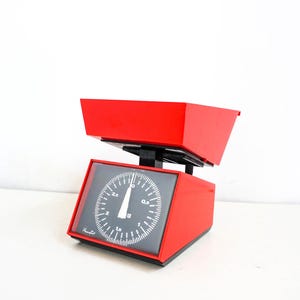 Op de afbeelding: Een rode keukenweegschaal met een zwarte wijzerplaat en een rode kom. De weegschaal heeft een maximale capaciteit van 2,5 kg.