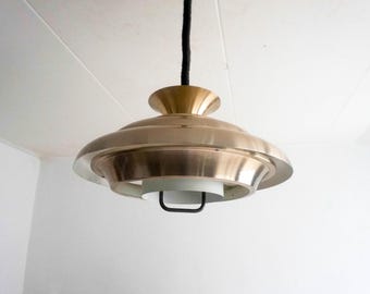 May include: A mid-century modern pendant light fixture with a circular, layered, brass-toned shade and a white diffuser.