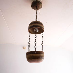 Op de afbeelding: Een vintage hanglamp met een tweekleurig, klokvormig ontwerp. De armatuur heeft een bruin en bronzen kleurenschema, met een zichtbare lamp in het bovenste gedeelte. De armatuur wordt opgehangen aan kettingen.