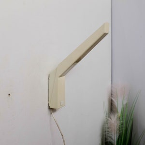 K&ouml;nnte beinhalten: Eine wei&szlig;e Wandleuchte mit einem langen, abgewinkelten Arm. Die Leuchte hat ein schlichtes, modernes Design und ist im minimalistischen Stil gehalten.