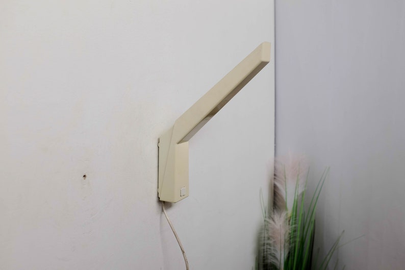 K&ouml;nnte beinhalten: Eine wei&szlig;e Wandleuchte mit einem langen, abgewinkelten Arm. Die Leuchte hat ein schlichtes, modernes Design und ist im minimalistischen Stil gehalten.