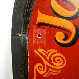 May include: Close-up of a red, round sign with black and gold lettering. The sign has a black wooden frame and a hole in the center.