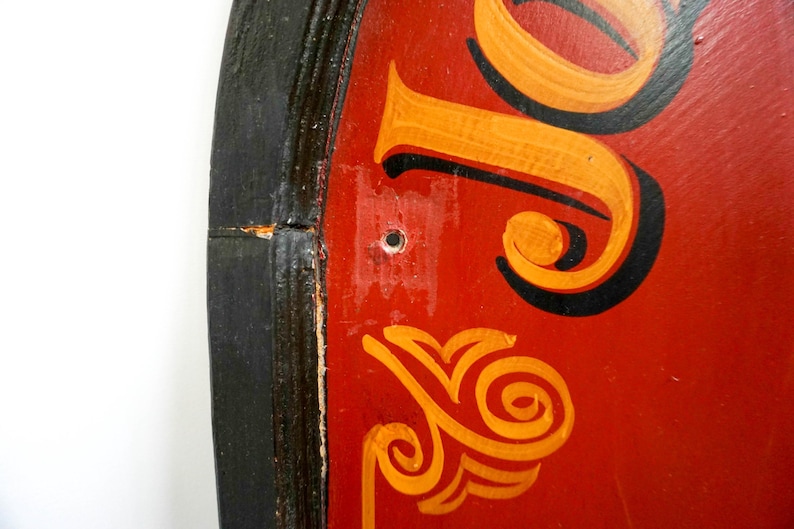 May include: Close-up of a red, round sign with black and gold lettering. The sign has a black wooden frame and a hole in the center.