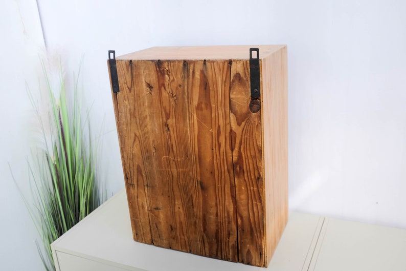 Op de afbeelding: Een houten kast met een rustieke bruine afwerking en zwarte metalen scharnieren. De kast heeft een eenvoudig ontwerp en is perfect voor het opbergen van kleine voorwerpen.