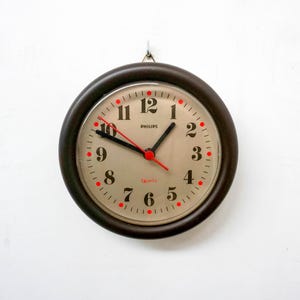 May include: A brown round wall clock with a white face and black numbers. The clock has a red second hand and the words "PHILIPS Quartz" printed on the face.