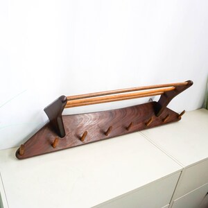 May include: A dark brown wooden wall-mounted coat rack with a curved shelf and five hooks. The rack has a mid-century modern design.