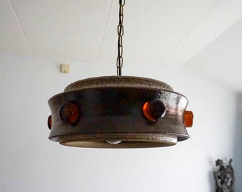 May include: A brown ceramic pendant light fixture with a round, layered design. The fixture has five amber glass accents around the edge.