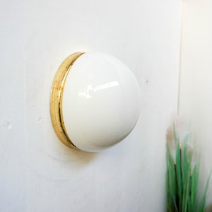 Peut inclure: Un luminaire de plafond blanc avec une bordure dorée. La lumière est montée sur un mur blanc.