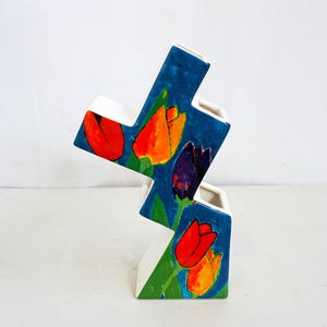 Op de afbeelding: Een witte keramische vaas met een blauwe achtergrond en een veelkleurig tulpenontwerp. De vaas is trapvormig met drie niveaus.