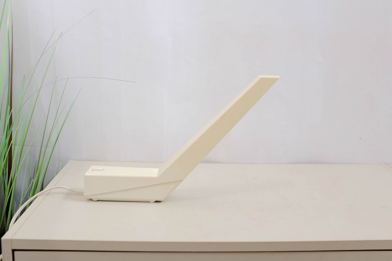 K&ouml;nnte beinhalten: Eine wei&szlig;e, eckige Tischlampe mit einem langen, d&uuml;nnen Arm. Die Lampe steht auf einer wei&szlig;en Oberfl&auml;che.