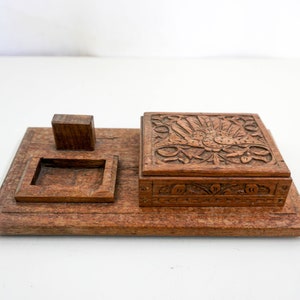 Puede incluir: Una caja de madera con tallas intrincadas, que presenta un diseño floral en la tapa y un compartimento más pequeño en el lateral. La caja está hecha de madera marrón oscura y tiene una forma rectangular.