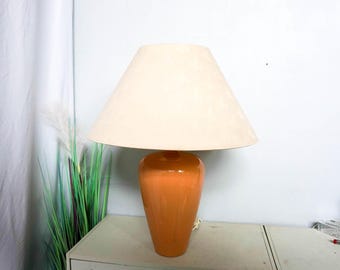 May include: A table lamp featuring a peach-coloured ceramic base and a cream-coloured lampshade. The lamp has a classic design, suitable for a living room or bedroom. The lampshade is cone-shaped.