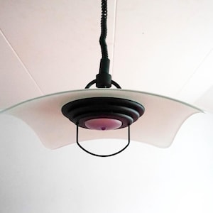 May include: A white glass ceiling light fixture with a black metal frame and a curved design. The light fixture has a single bulb in the center.