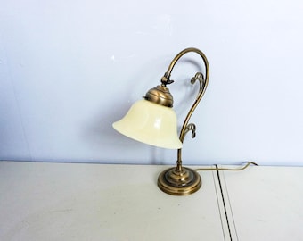Peut inclure: Une lampe de bureau vintage en laiton avec un bras incurvé et un abat-jour en verre de couleur crème. La lampe a une base ronde et des ornements décoratifs. Le cordon est visible. C'est un élément de décoration intérieure classique.