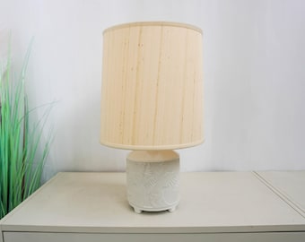 Può includere: Lampada da tavolo in ceramica bianca con paralume in lino bianco. La base della lampada presenta un design a foglie in rilievo.