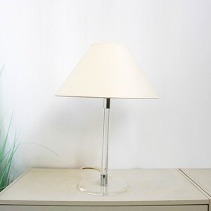 May include: A white lampshade with a clear acrylic base and a chrome stem. The lamp is on a white surface.