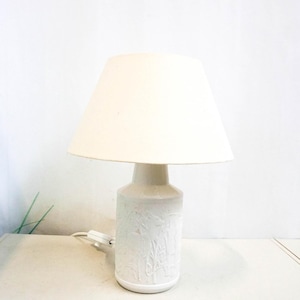 Puede incluir: Lámpara de mesa de cerámica blanca con una pantalla de tela blanca. La base de la lámpara tiene un diseño en relieve.