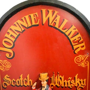 May include: A vintage wooden sign with a red background and black trim. The sign features the text "Johnnie Walker Scotch Whisky" in gold lettering. The sign is shaped like an arch and has a decorative design around the edges.