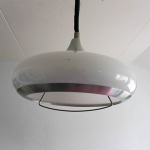 May include: A white and silver pendant light with a round, saucer-shaped shade. The light is suspended from the ceiling by a black cord.