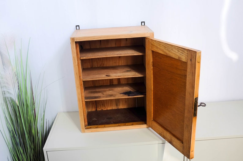 Op de afbeelding: Een houten wandkast met een enkele deur en vier planken. De deur staat open en de kast is leeg.