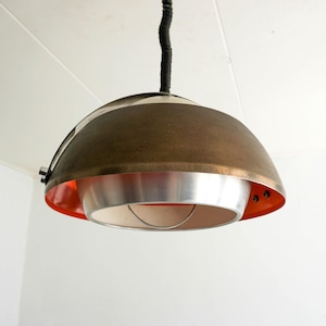 Op de afbeelding: Een moderne hanglamp uit het midden van de eeuw met een messing en zilveren afwerking. De lamp heeft een koepelvorm met een rode accent ring.