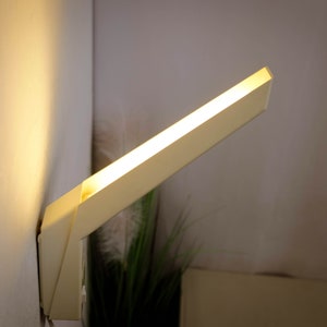 K&ouml;nnte beinhalten: Eine wei&szlig;e, rechteckige Wandleuchte mit warmwei&szlig;em Licht.