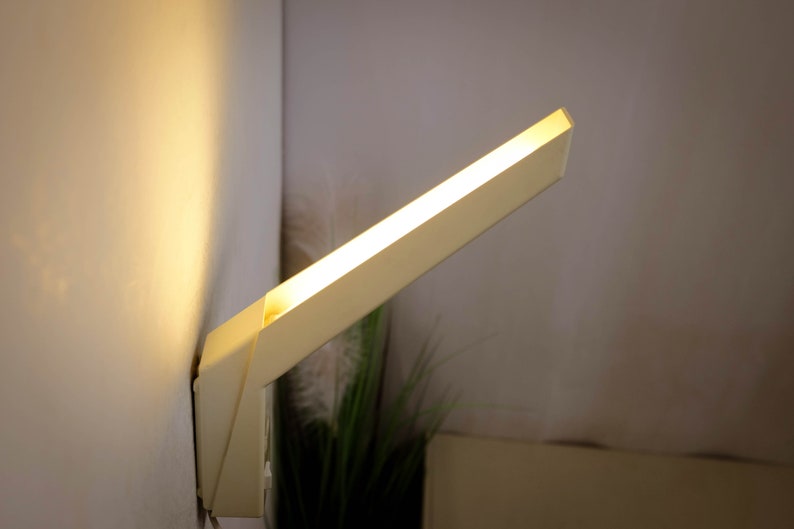 K&ouml;nnte beinhalten: Eine wei&szlig;e, rechteckige Wandleuchte mit warmwei&szlig;em Licht.