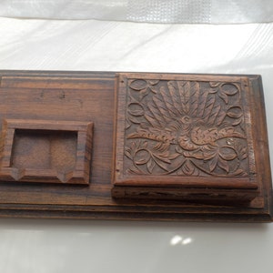 Puede incluir: Una caja de madera con un diseño tallado de un pájaro con las alas extendidas. La caja tiene un compartimento separado para guardar objetos pequeños.