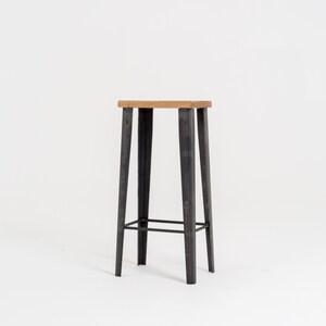 May include: A black metal bar stool with a wooden top. The stool has a simple design with four legs and a single crossbar for support.
