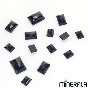 Puede incluir: Una colección de cabujones de piedras preciosas negras, cortados en forma rectangular, dispuestos sobre una superficie blanca.
