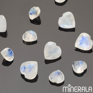 Puede incluir: Una colección de diez piedras de luna en forma de corazón. Las piedras son translúcidas y tienen un color blanco lechoso con destellos azules iridiscentes.