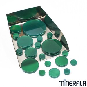 May include: A collection of green agate cabochons of various sizes in a metal tray. The cabochons are smooth and polished, with a translucent green color.