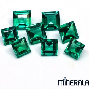 May include: A group of eight emerald green square-shaped gemstones on a white background.