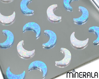 Könnte beinhalten: Eine Sammlung von 17 halbmondförmigen Opal-Cabochons. Die Cabochons sind eine Mischung aus weißem und hellblauem Opal. Die Cabochons sind auf einer silbernen Oberfläche angeordnet.