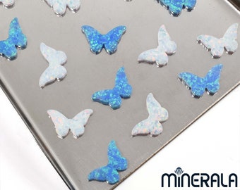 Könnte beinhalten: Sortiment aus schillernden blauen und weißen Opal-Schmetterlingsanhängern. Die Anhänger sind auf einer silbernen Oberfläche verstreut.