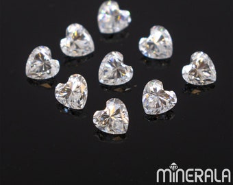 May include: A collection of heart-shaped, clear gemstones. The gemstones are arranged on a black surface, reflecting light and creating a sparkling effect. The image includes the "MINERALA" logo in white.
