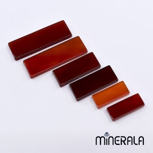 Peut inclure: Six pierres de cornaline rectangulaires de tailles différentes, disposées en diagonale du plus grand au plus petit. Les pierres sont d'une couleur rouge foncé avec des nuances orangées.