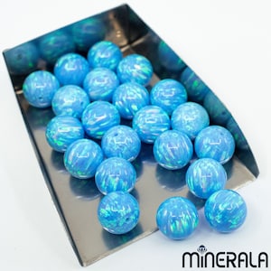 May include: A tray of blue opal beads. The beads are round and have an iridescent sheen. The beads are arranged in a random pattern on the tray.