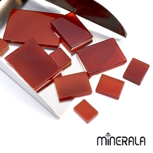 Peut inclure: Plusieurs pierres précieuses de cornaline polies, de forme rectangulaire et de tailles variées. Les pierres, d'un brun rougeâtre translucide, sont disposées sur un plateau argenté. L'image met en valeur les surfaces lisses et les couleurs naturelles des pierres.