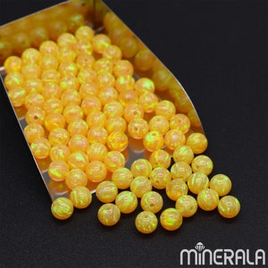 May include: A large pile of yellow opal beads with a green iridescent sheen. The beads are round and smooth, and they are scattered on a silver tray.