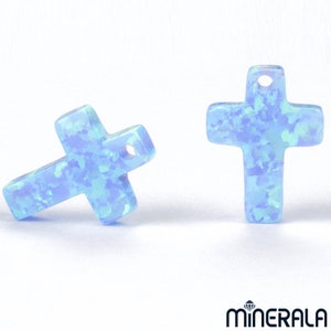 May include: Two light blue opal cross charms with a hole at the top for hanging. The crosses have a sparkly, iridescent finish.