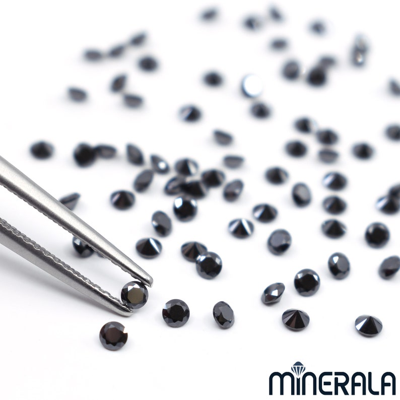 May include: A close-up of a pair of tweezers holding a black diamond gemstone. Several other black diamonds are scattered on a white surface.