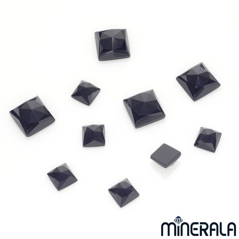 Puede incluir: Un conjunto de gemas negras talladas en forma cuadrada y facetadas, de diferentes tama&ntilde;os, sobre una superficie blanca. Las gemas tienen una superficie pulida y reflectante, sugiriendo una exhibici&oacute;n de piedras sueltas.