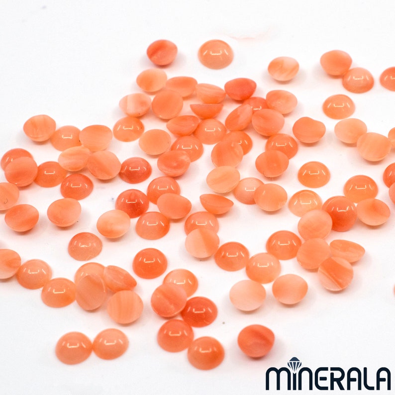 Pu&ograve; includere: Una collezione di circa 50 piccole pietre di corallo rosa di forma rotonda e cabochon. Le pietre sono lisce e lucidate, con un leggero bagliore.