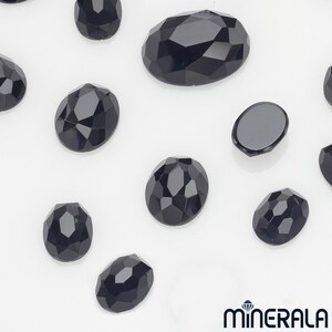 Peut inclure: Assortiment de strass noirs de forme ovale facet&eacute;s. Les strass sont de diff&eacute;rentes tailles et sont dispos&eacute;s sur une surface blanche.