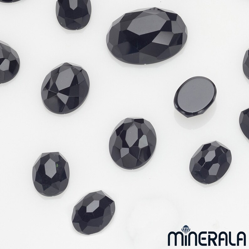 Peut inclure: Assortiment de strass noirs de forme ovale facet&eacute;s. Les strass sont de diff&eacute;rentes tailles et sont dispos&eacute;s sur une surface blanche.